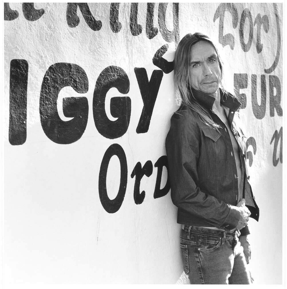 Iggy Pop lehnt an einer Wand mit der Aufschrift IGGY