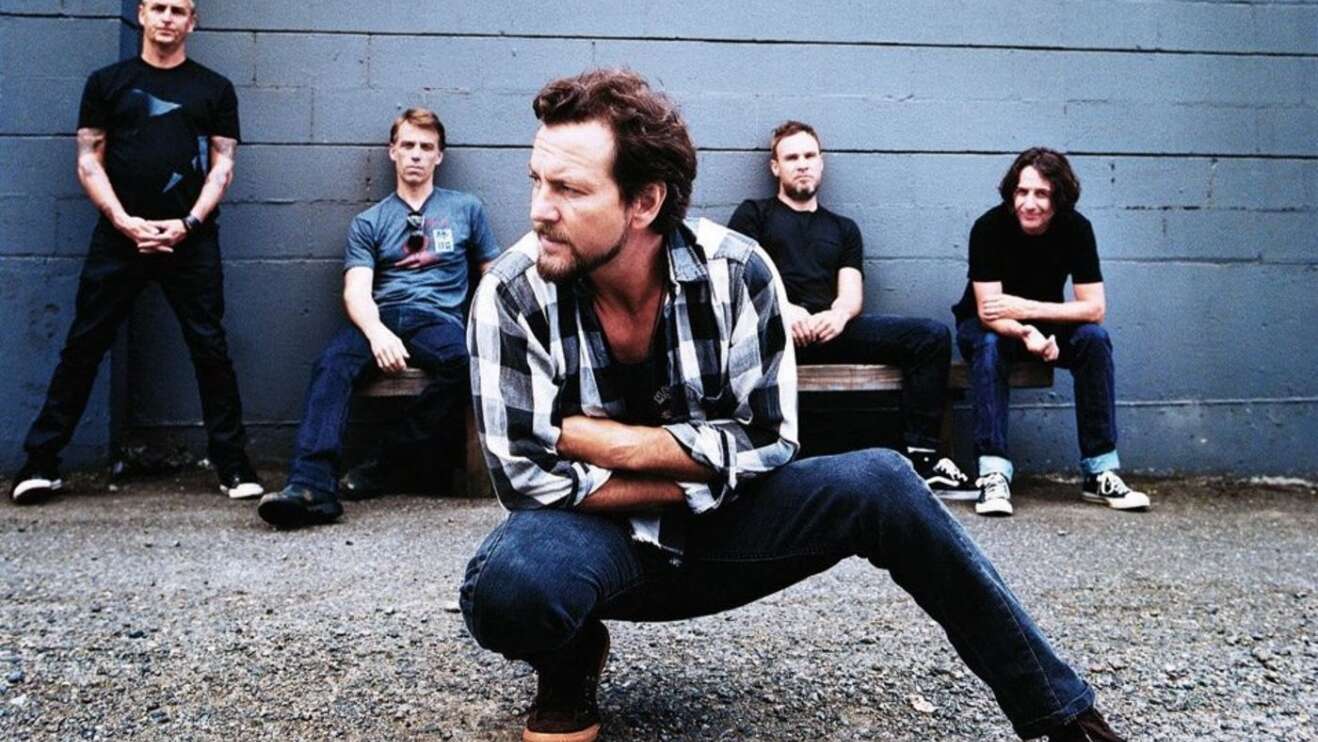 Pearl Jam posieren kniend und sitzend vor grauer Steinmauer