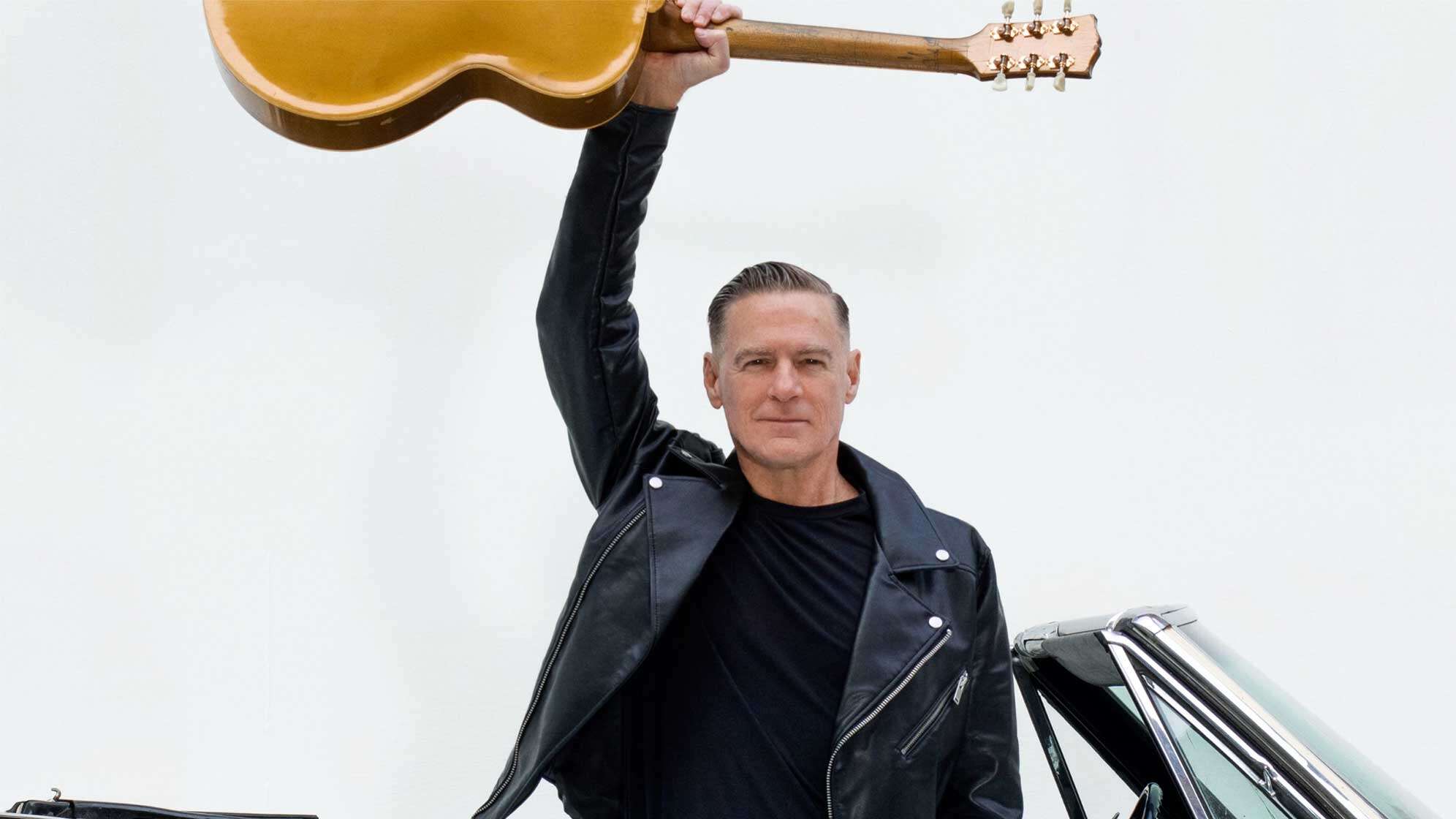 Ein Foto von Bryan Adams, wie er seine Gitarre in die Höhe hält