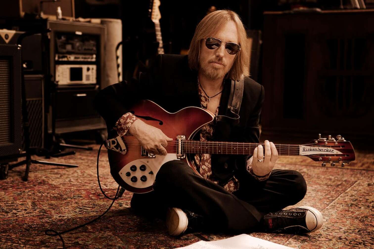 Tom Petty sitzt mit Gitarre auf dem Boden