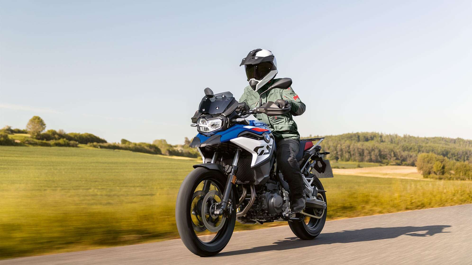 Ein Motorradfahrer fährt eine BMW Motorrad R 1300 GS auf einer Straße in idyllischer Wiesenlandschaft