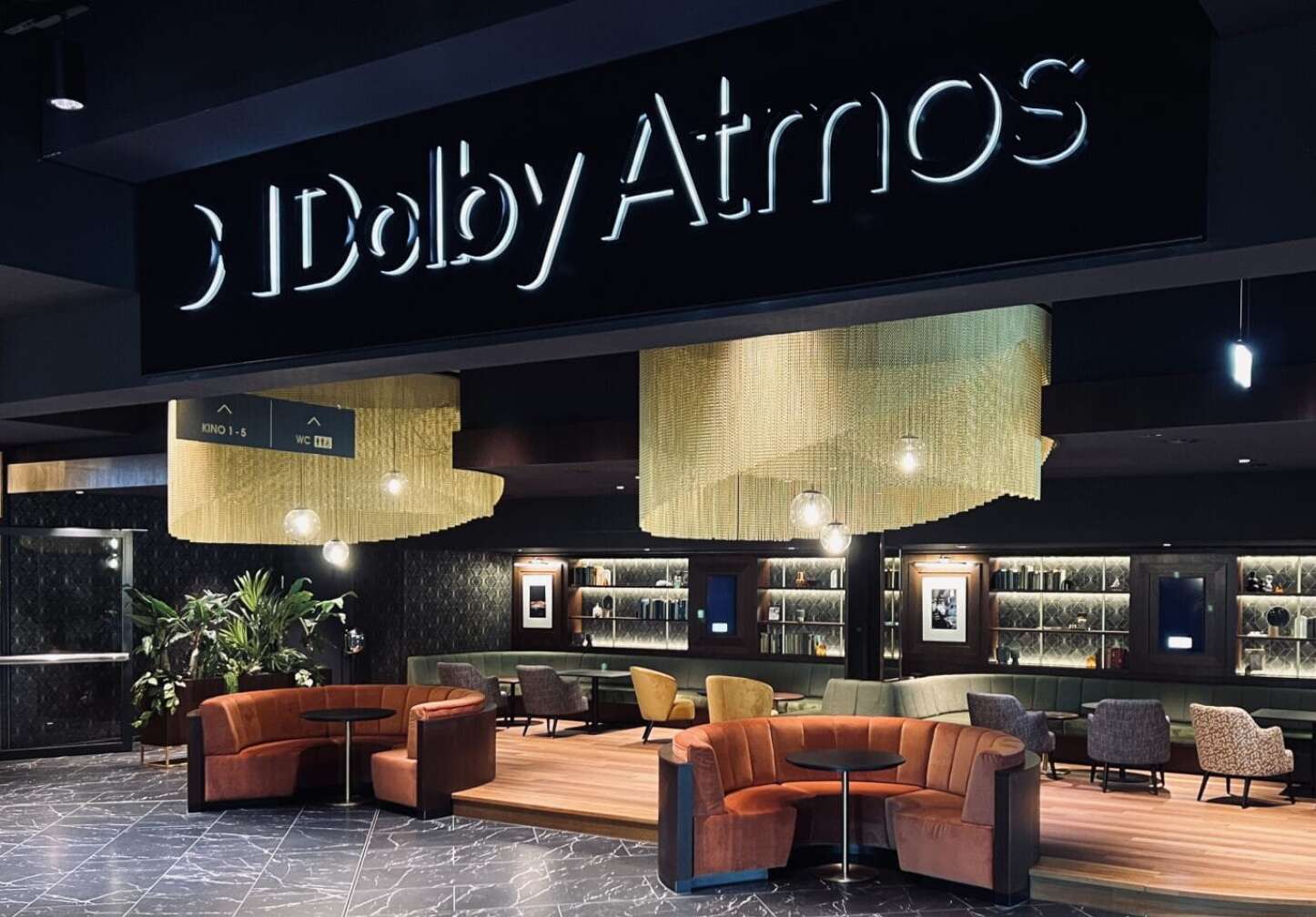 Foto eines leeren Kinofoyers, zu sehen ist ein Leuchtschild für Dolby Atmos und ein paar bequeme Sessel